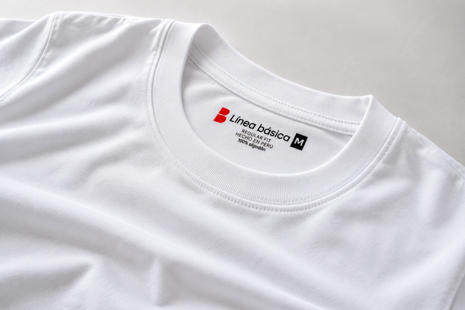 Primer plano del cuello de un polo blanco con la etiqueta Línea básica: regular fit, hecho en Perú, 100% algodón